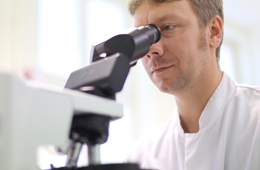 Mann in weißem Kittel schaut in Mikroskop im Institut für Mikrobiologie der Uniklinik Rostock